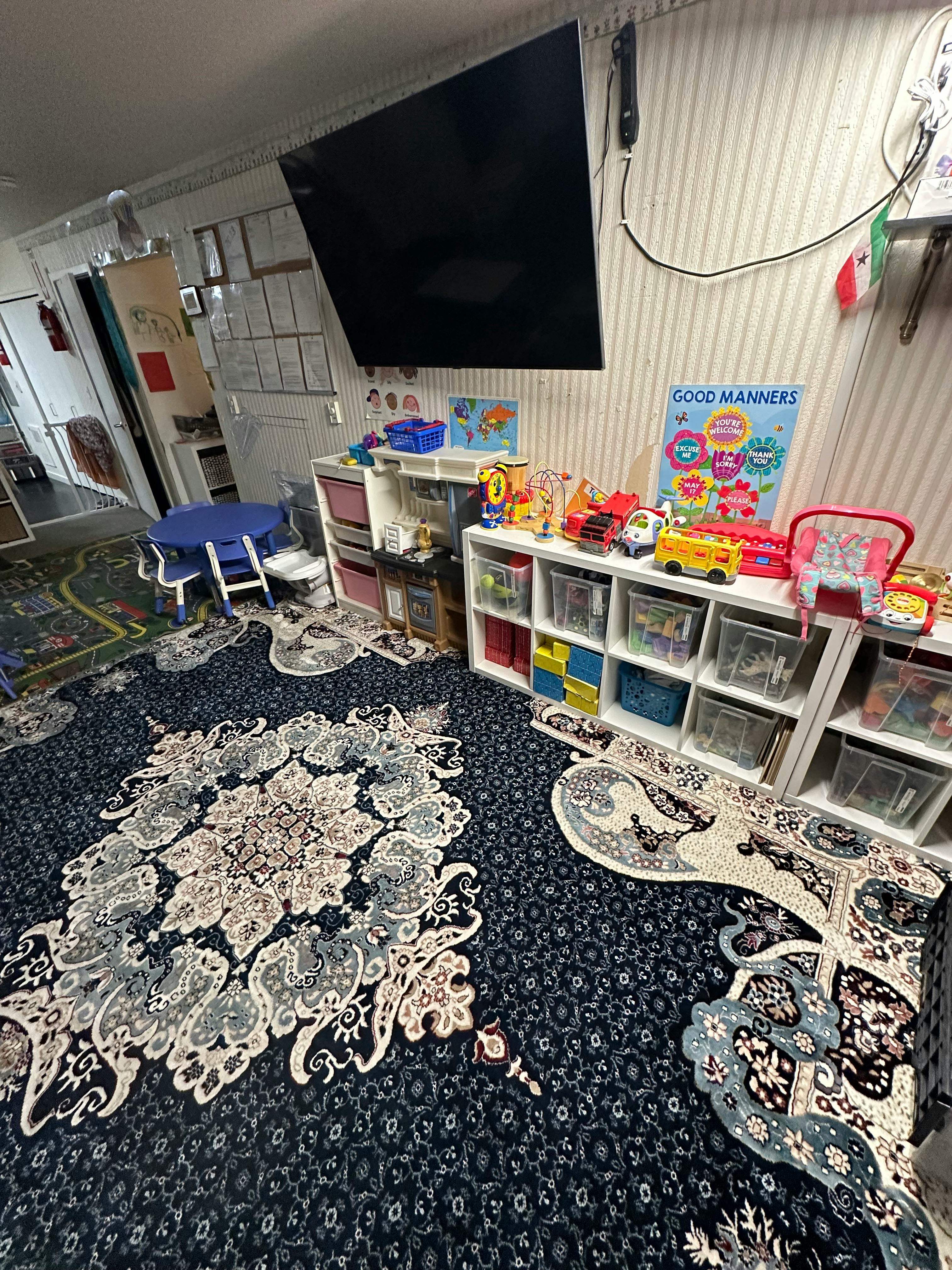 Playroom with toys on shelves, a small blue table and chairs, and patterned rugs