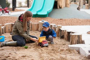 Person and child playing with toy truck in sandbox