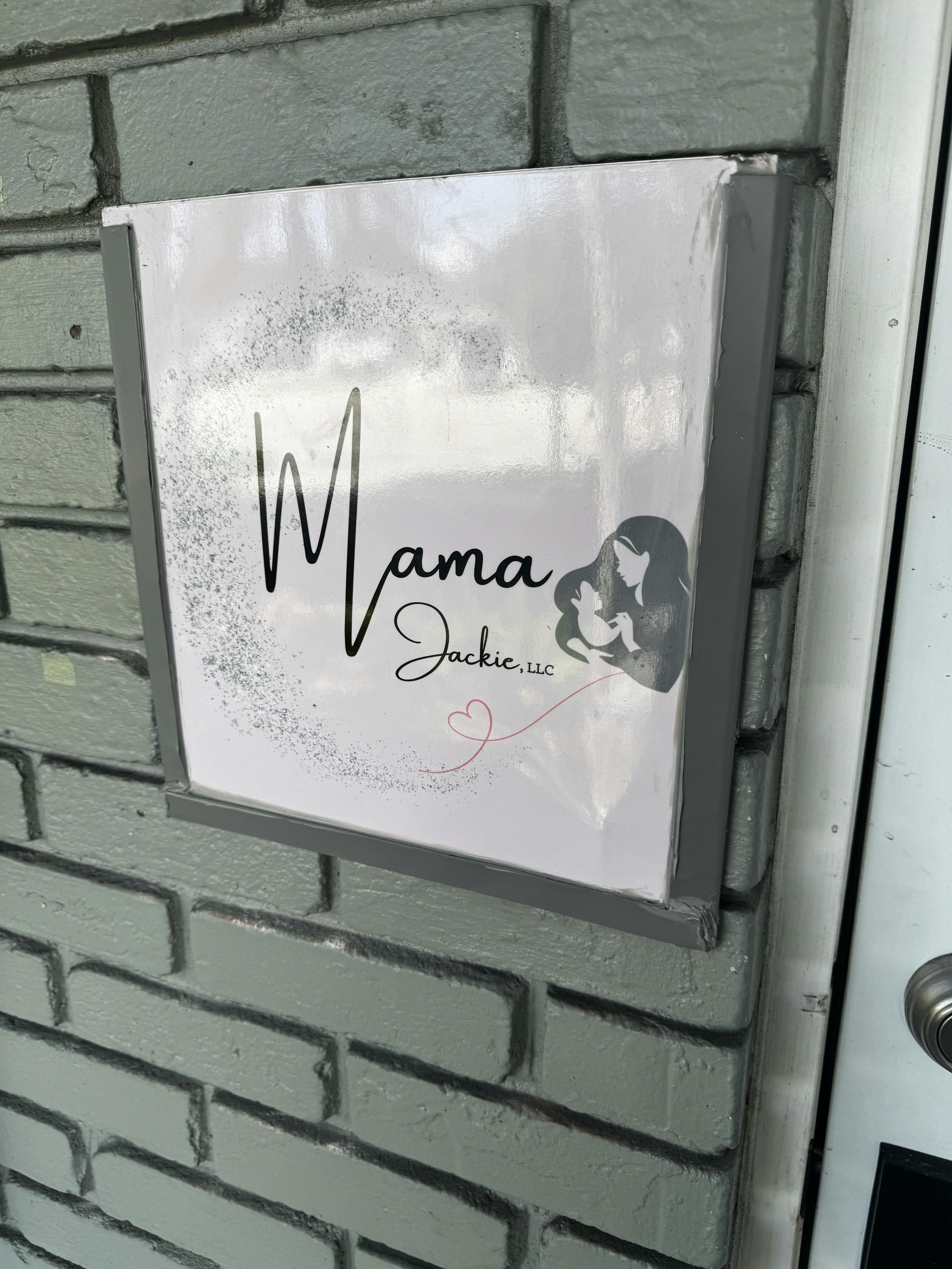 Sign on a gray brick wall with the text Mama Jackie, LLC and an illustration