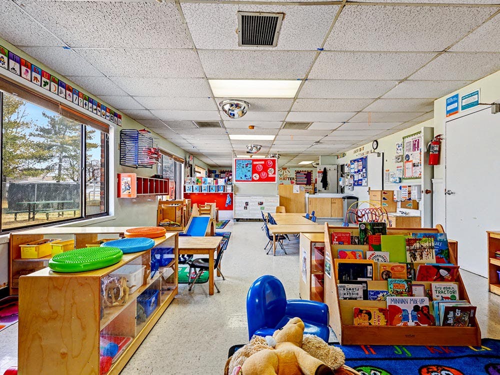 Empty classroom with small tables and chairs, shelves of toys and books