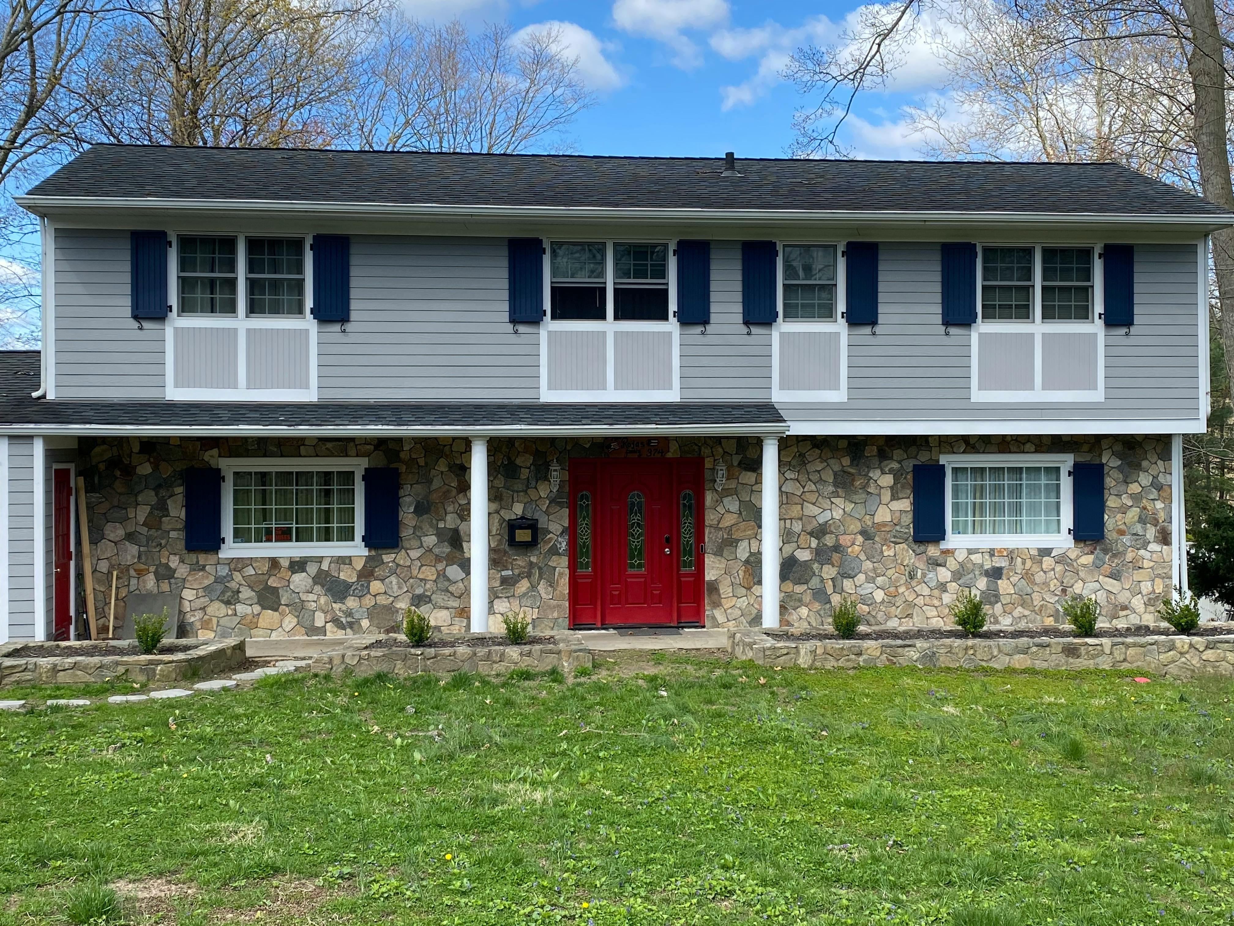 Two-story house with gray siding, stone facade, and red front door