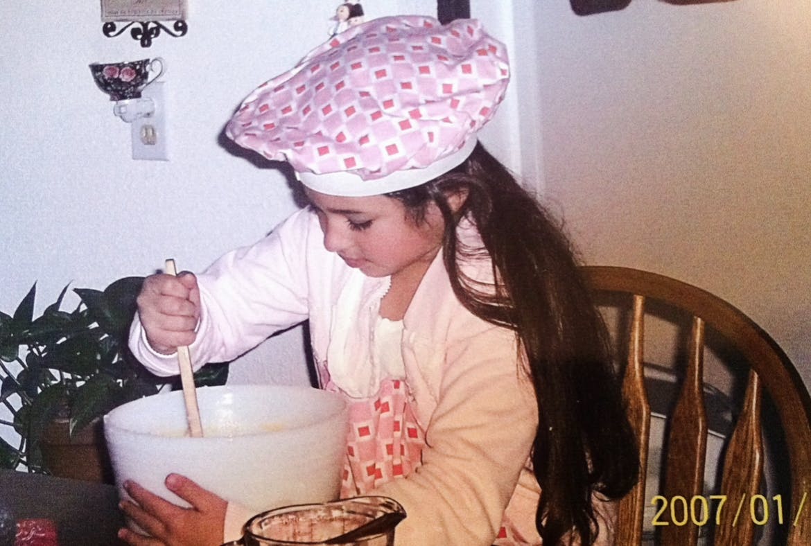 Child in a chef hat stirring a bowl in a kitchen
