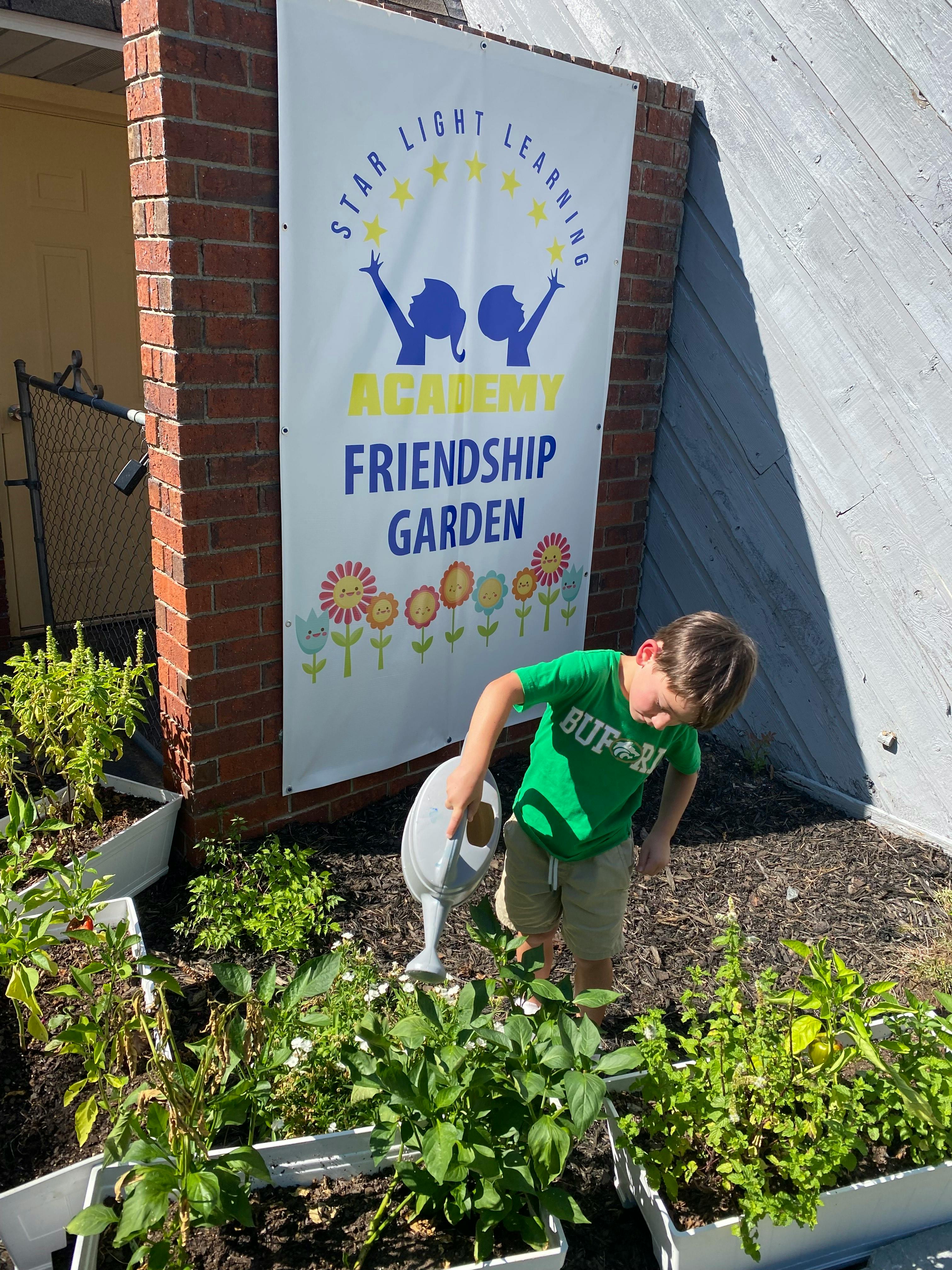 Child watering plants in a garden next to a sign for "Friendship Garden"