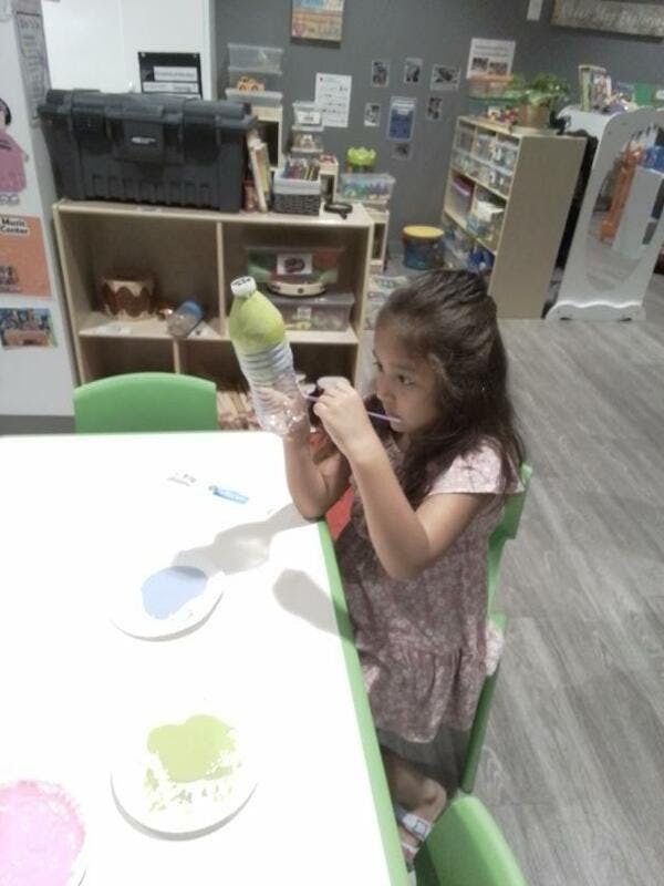 Child sitting at a table, holding a plastic bottle and a small brush
