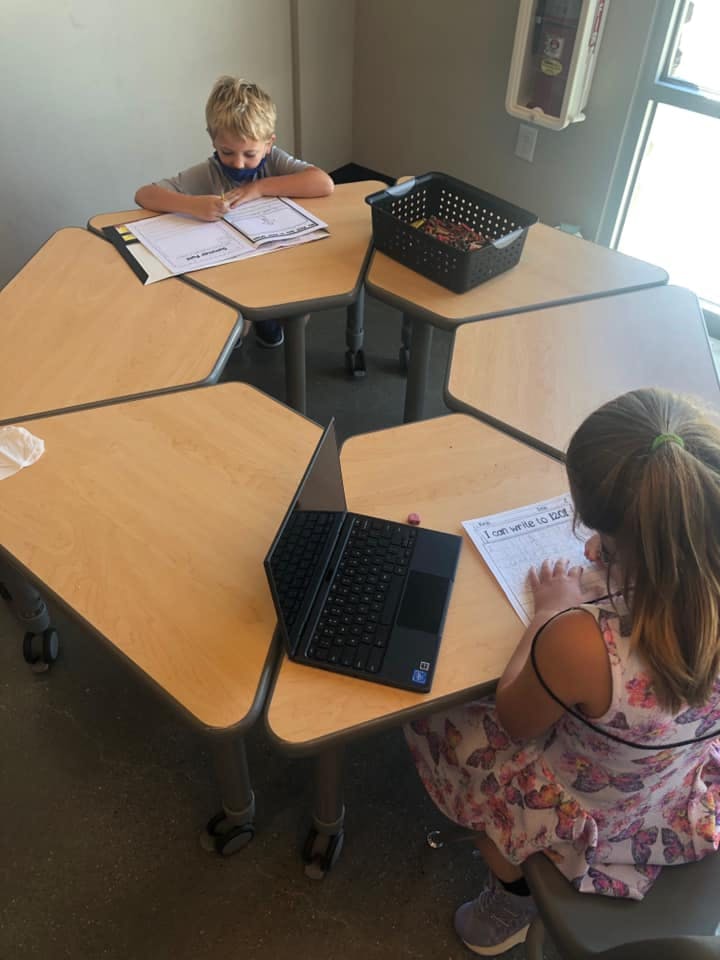 Two children working at a hexagonal table in a classroom