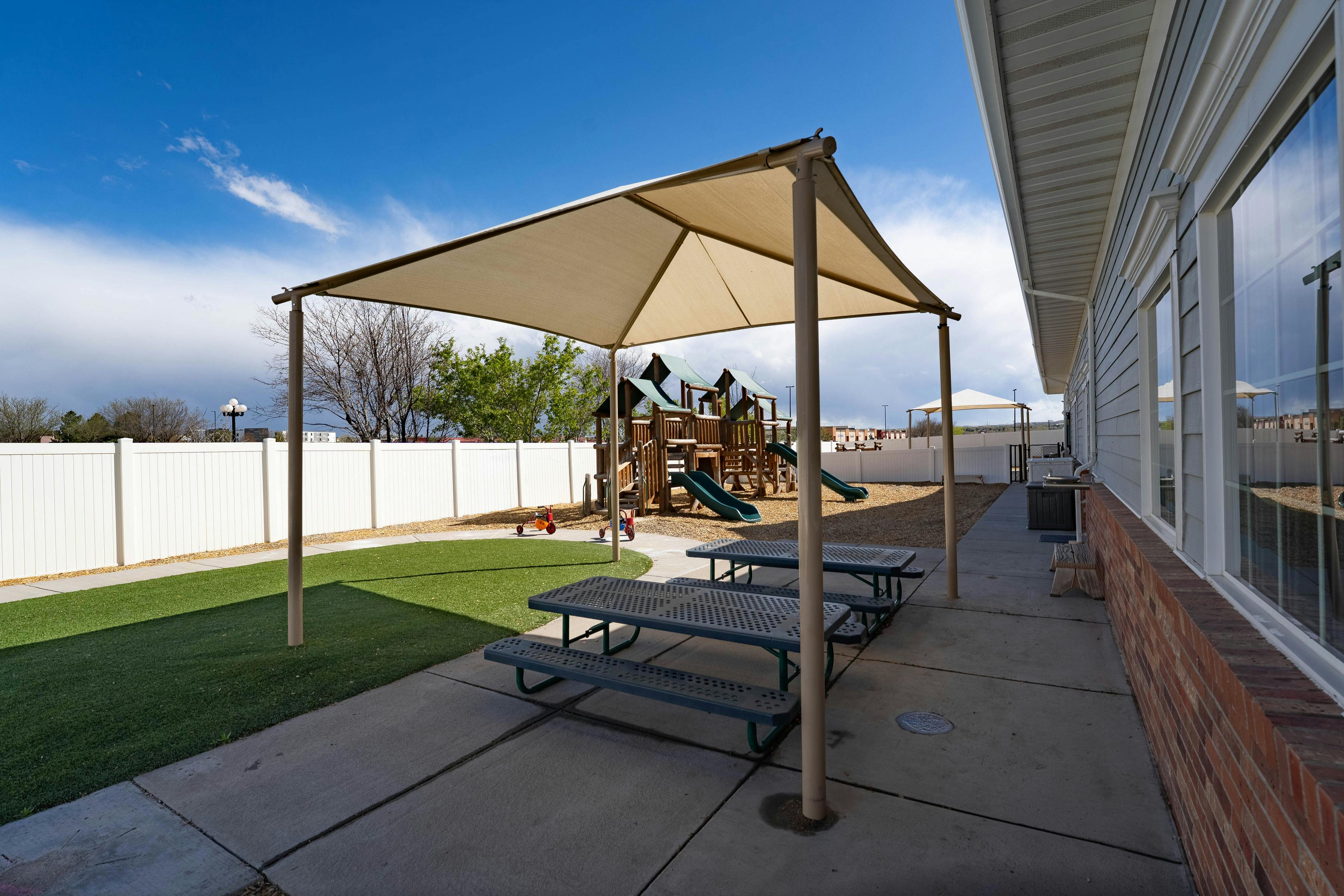 Covered picnic tables next to artificial grass and a playground
