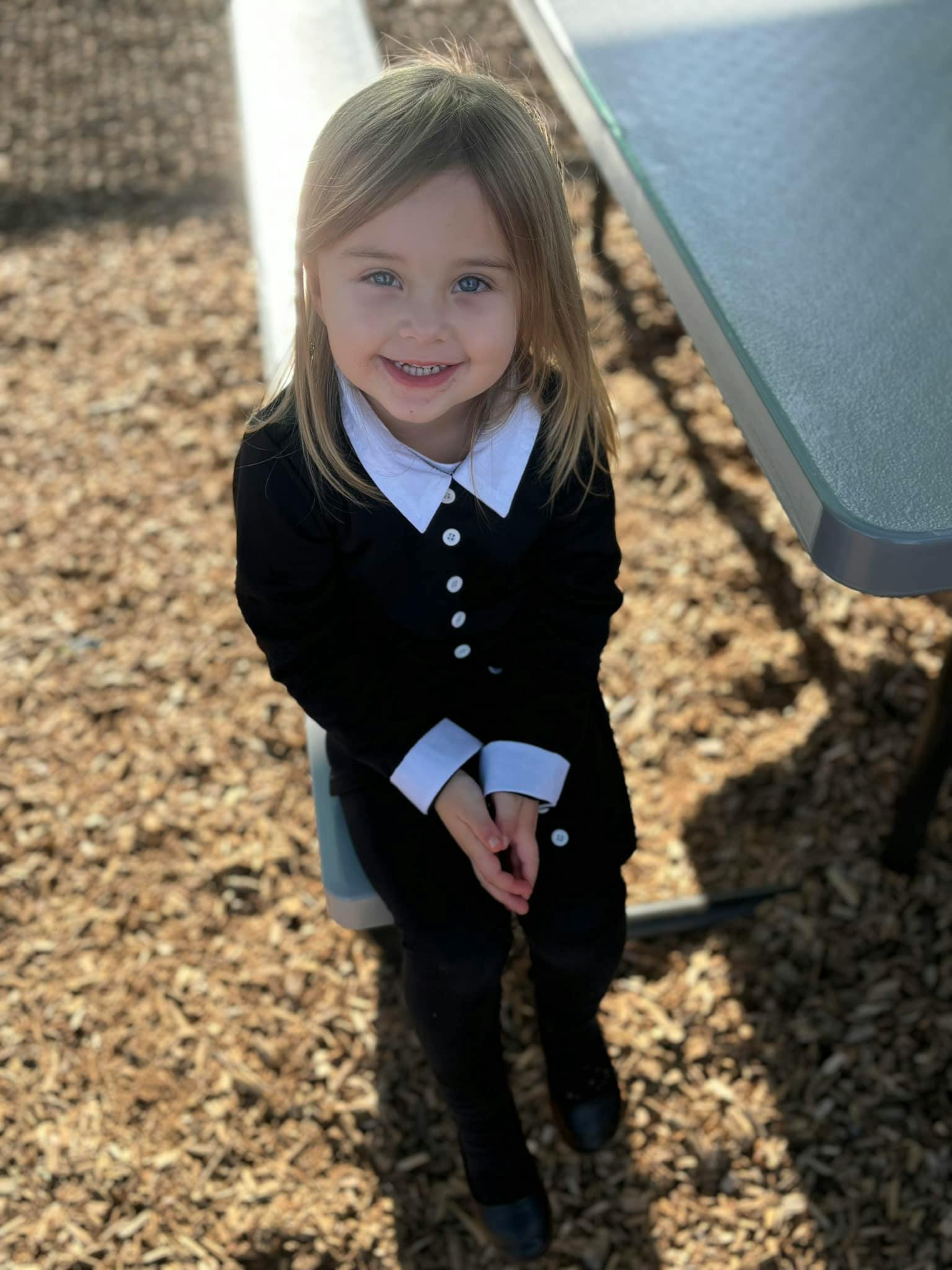Child in a black suit with a white collar sitting outdoors