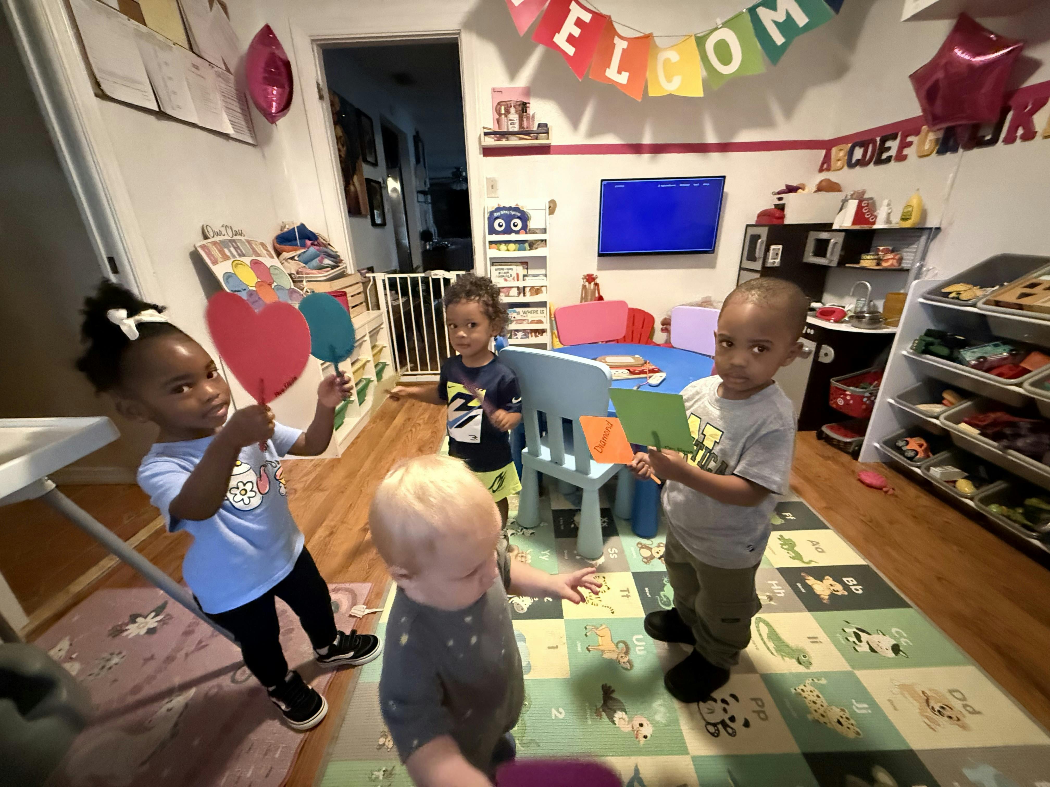 Four young children playing in a classroom with toys and learning materials