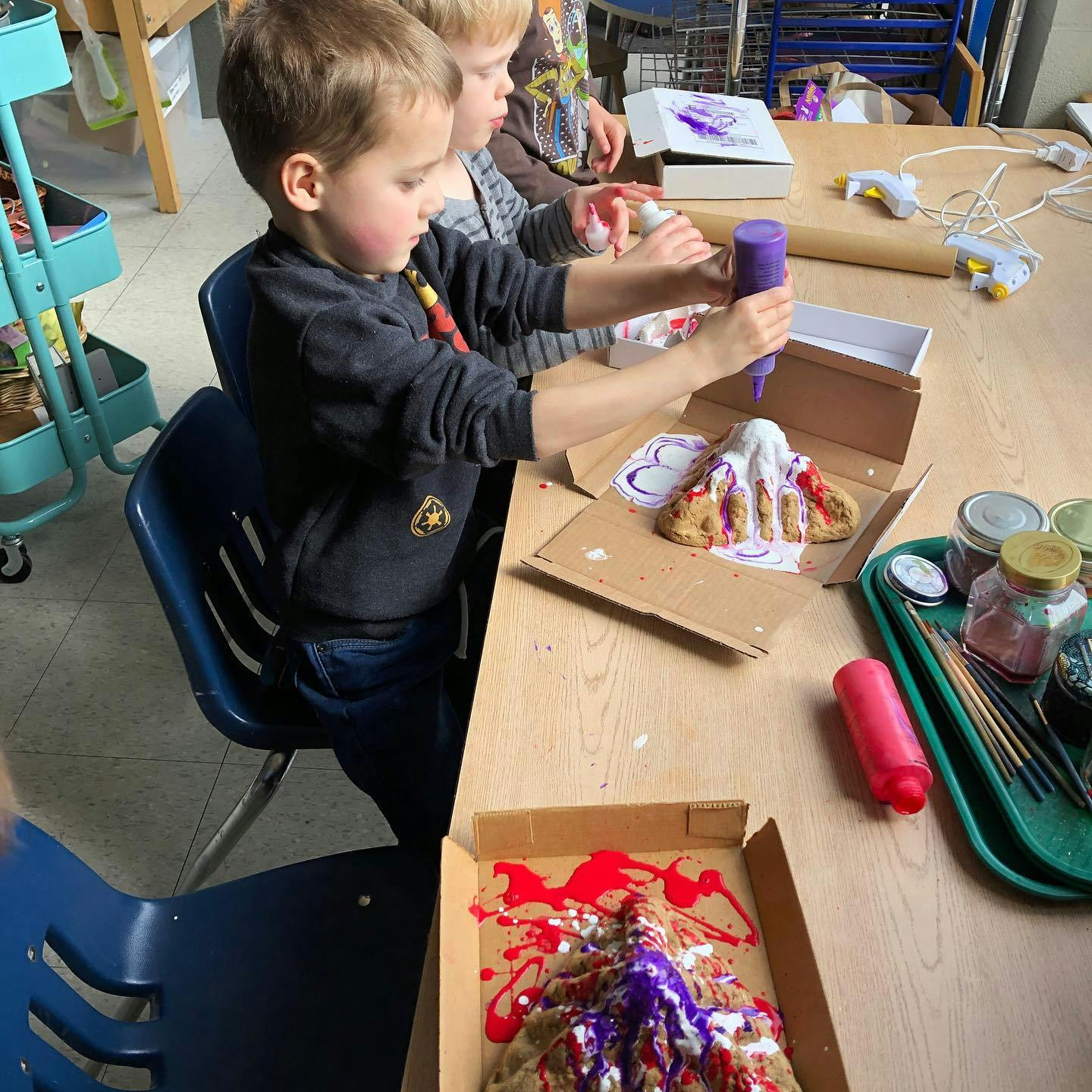 Child squeezing purple paint onto a volcano craft