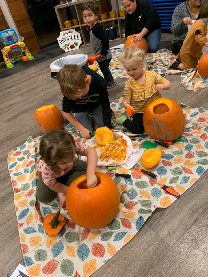 Children carving pumpkins on a leaf-patterned blanket