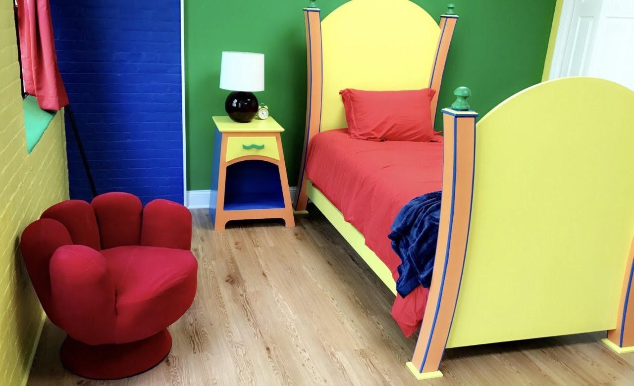 Bedroom with yellow bed, red bedding, red chair, and nightstand