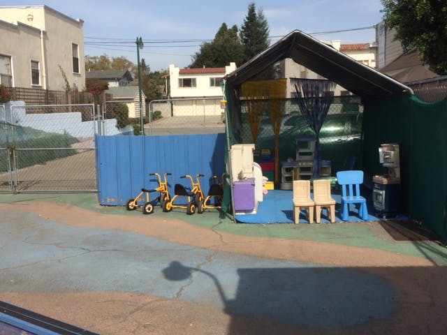 Outdoor play area with small tricycles and a covered structure with chairs