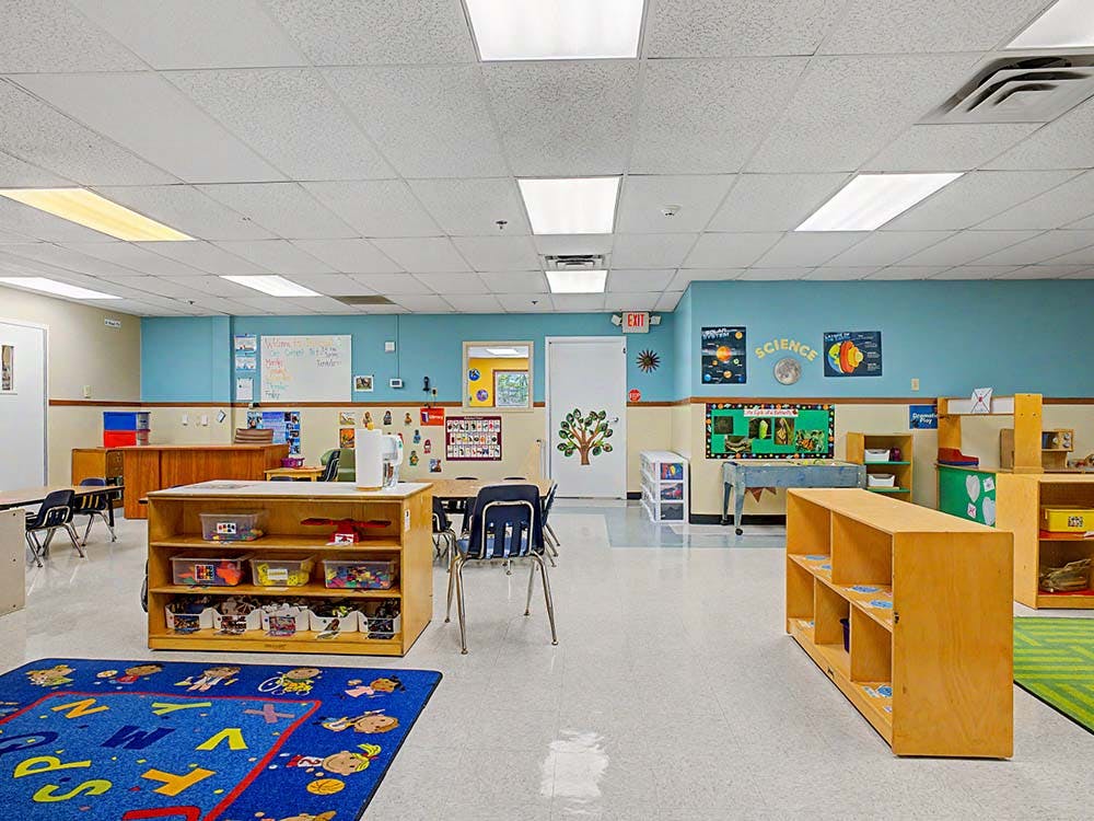 Empty classroom with colorful decor, shelves, tables, and a blue alphabet rug