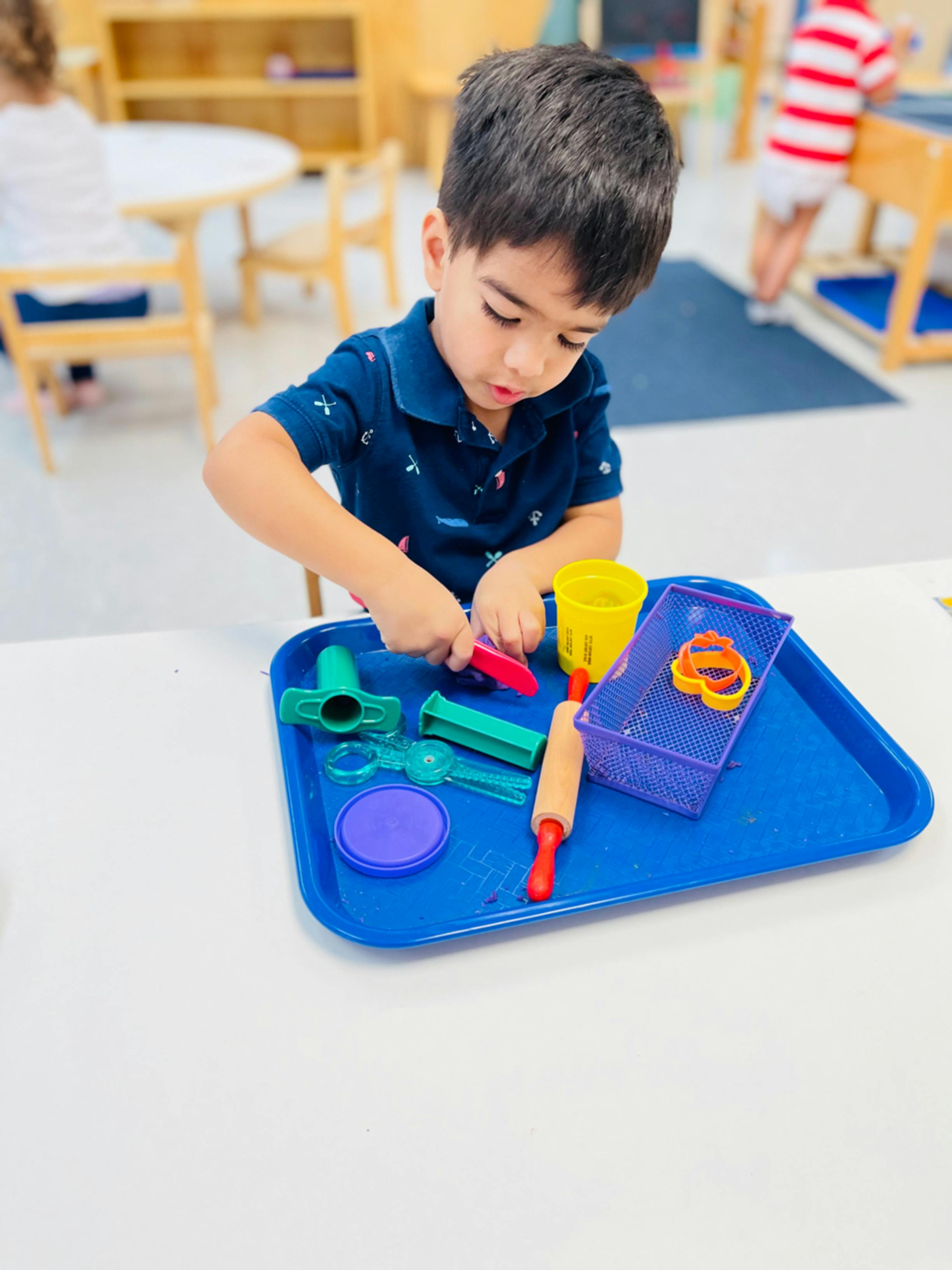 Child playing with colorful toys on a blue tray in a classroom