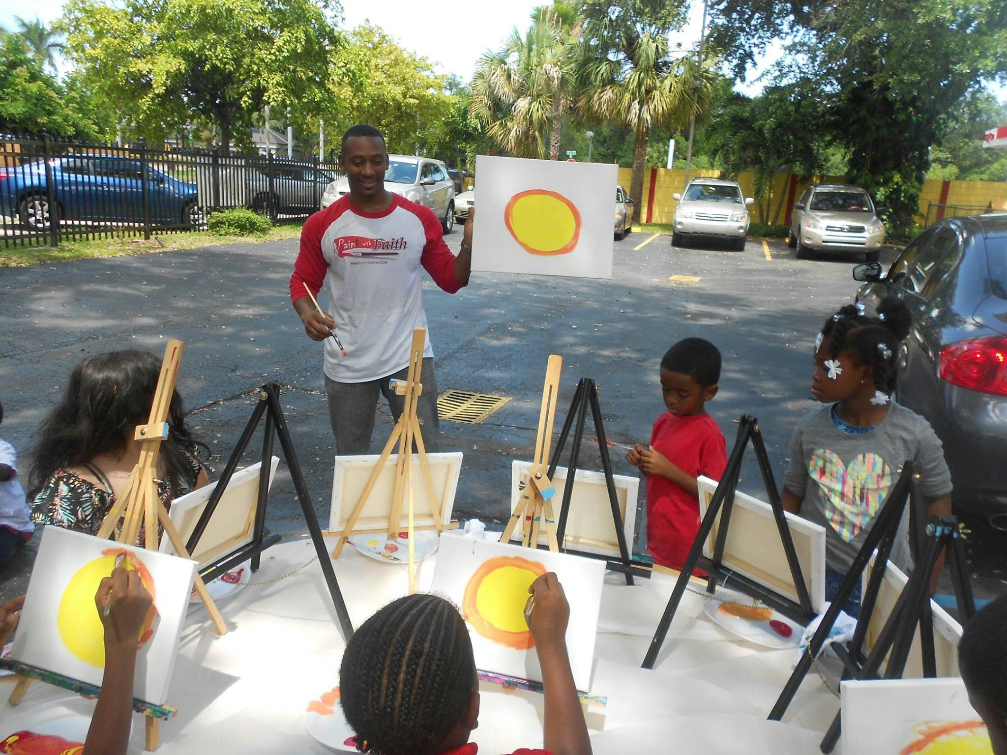 Person teaching children to paint yellow circles on canvases outdoors
