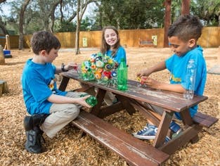 Three children playing with crafts at a picnic table outdoors