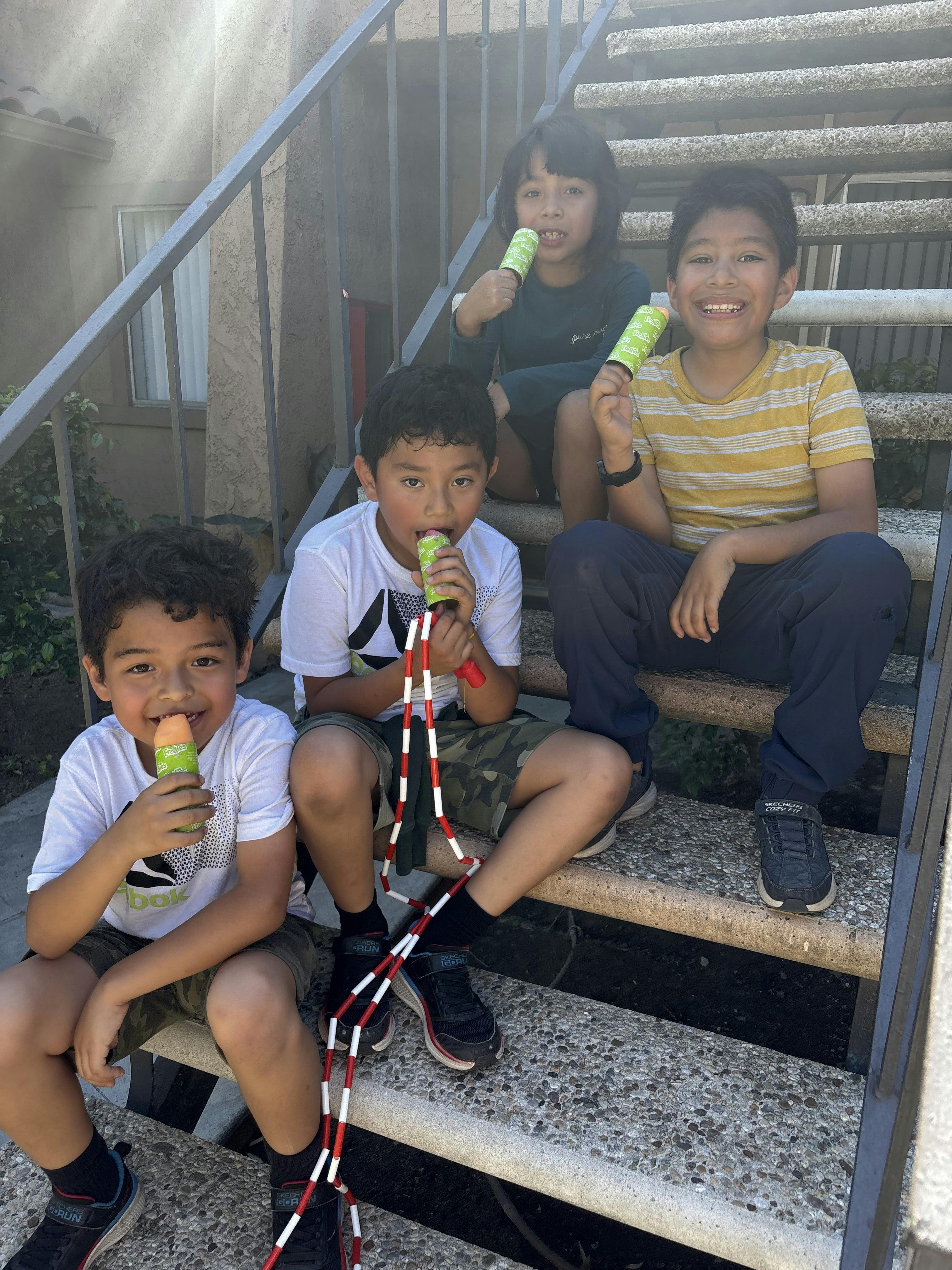 Four children sitting on outdoor steps, eating push pops and pop candy