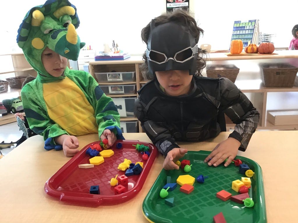 Two children in costumes playing with colorful blocks at a table