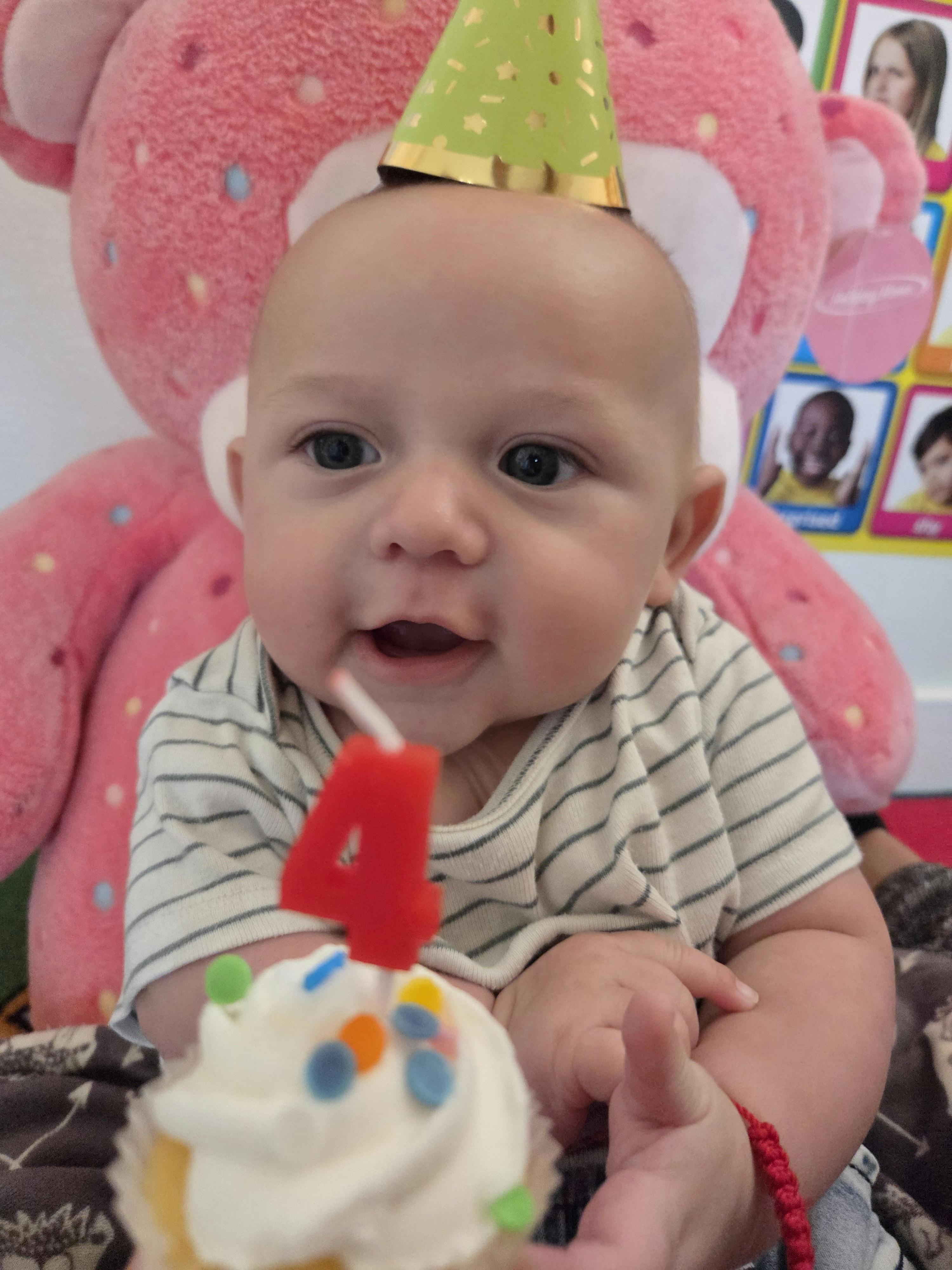Child wearing a party hat with a cupcake featuring a number four candle