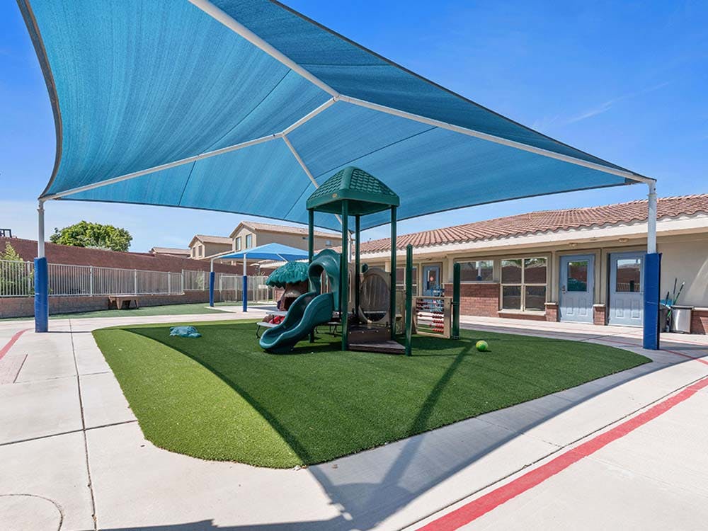 Playground area with green turf and a blue shade structure