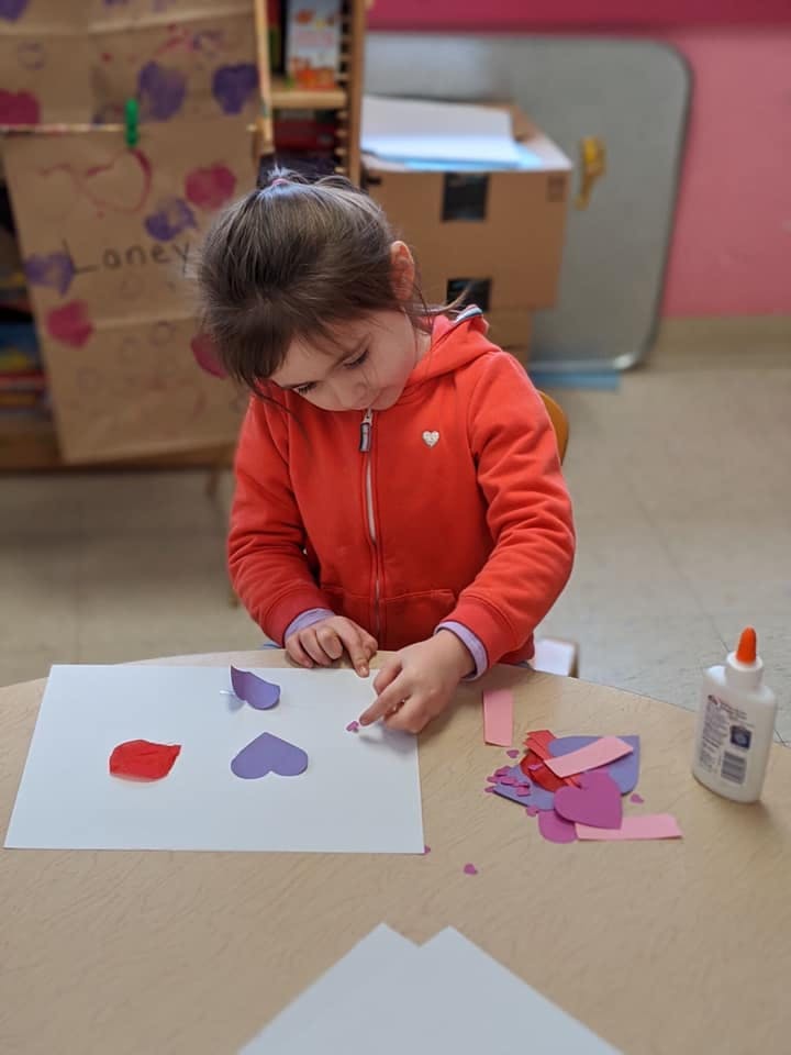 Child gluing paper hearts onto a white sheet