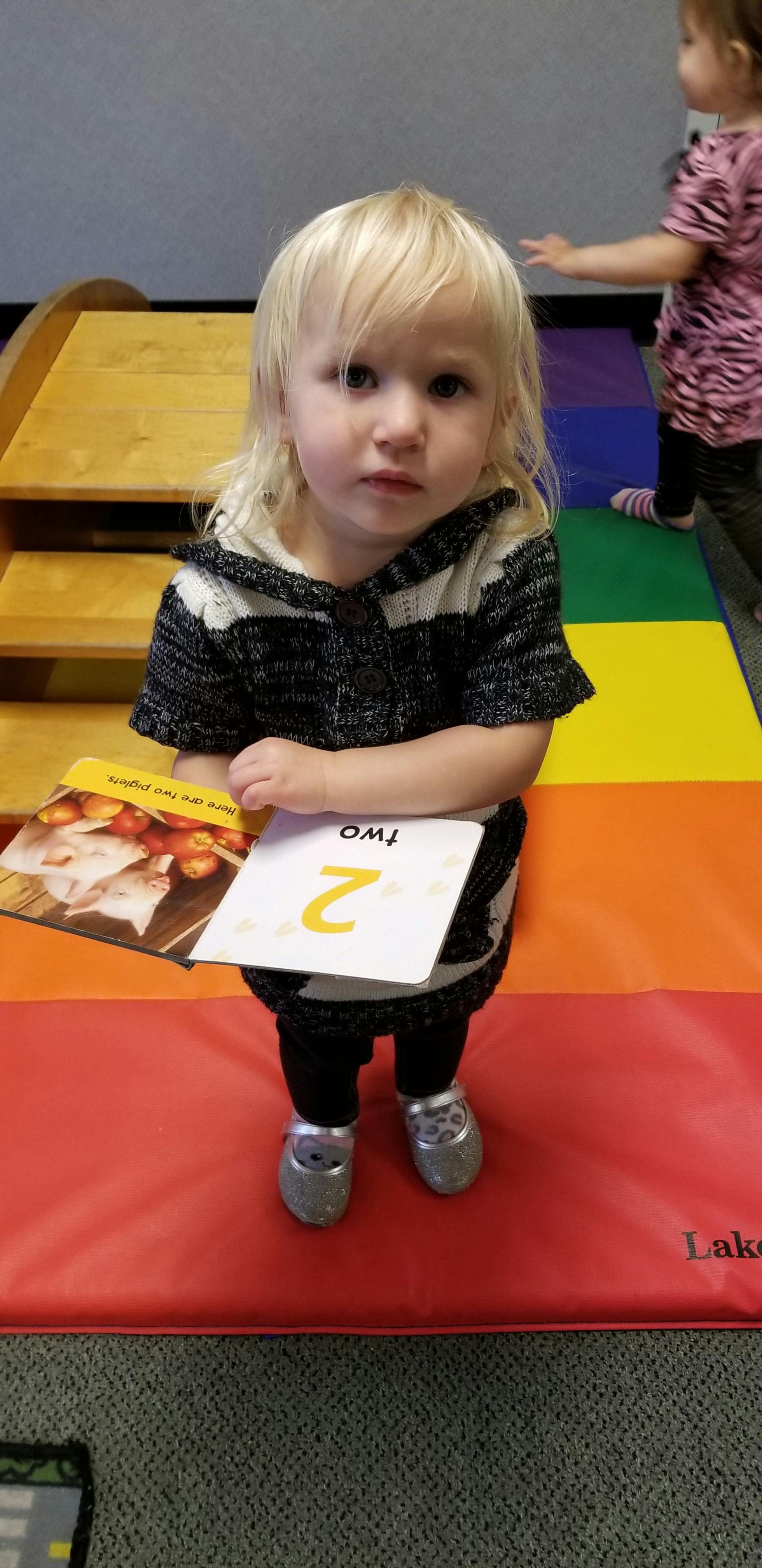 Child holding a book and a flashcard with the number 2