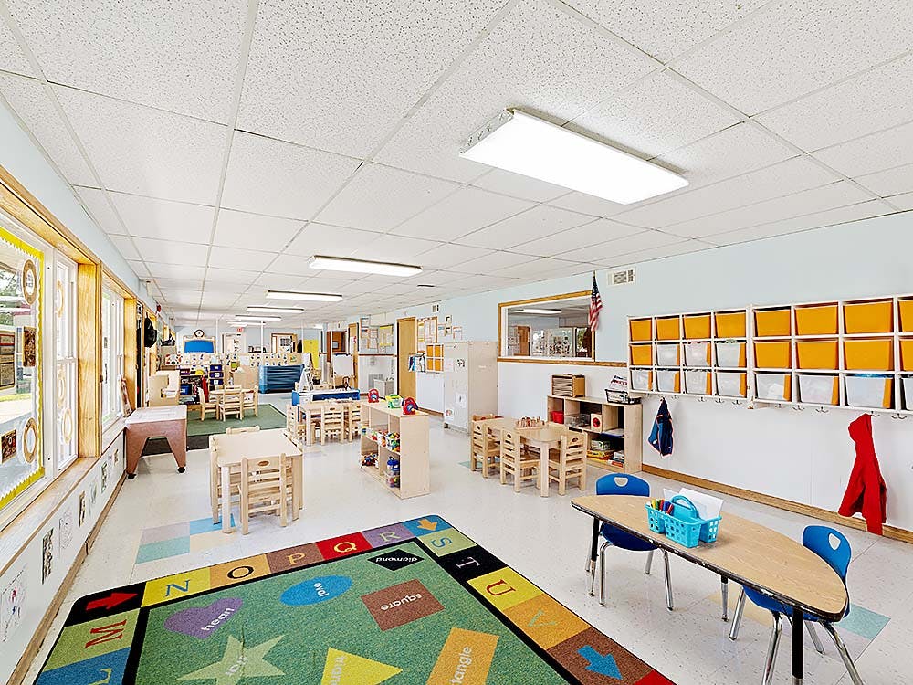 Empty preschool classroom with small tables and chairs and a colorful ABC rug