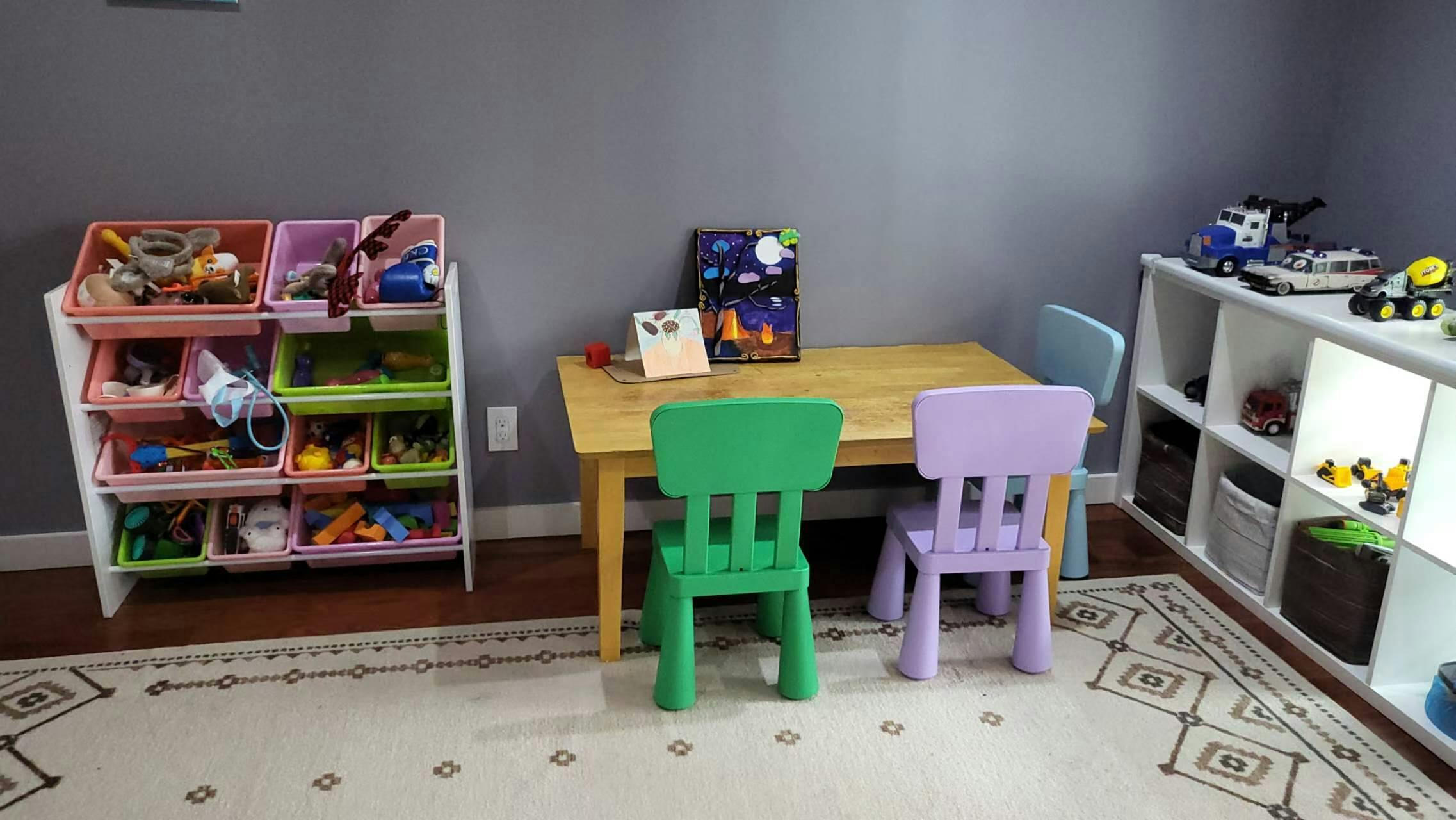 A playroom with a small table and chairs, toy storage, and a white shelf with toys