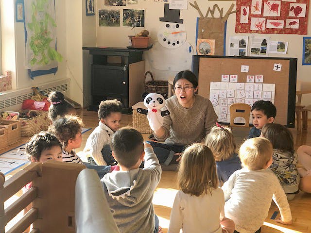 Person with a panda puppet talking to a group of children in a classroom