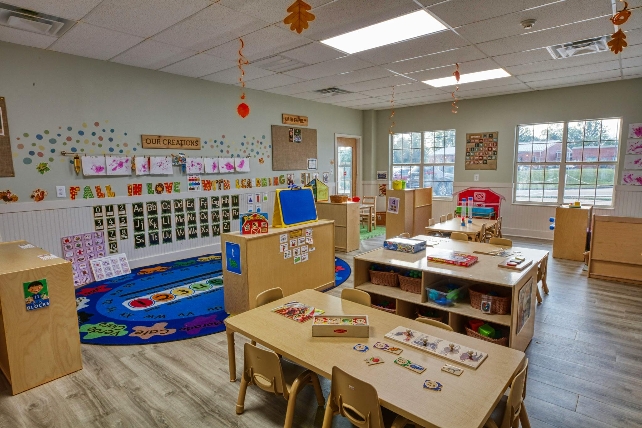 An empty early childhood classroom with multiple small tables, chairs, and learning materials