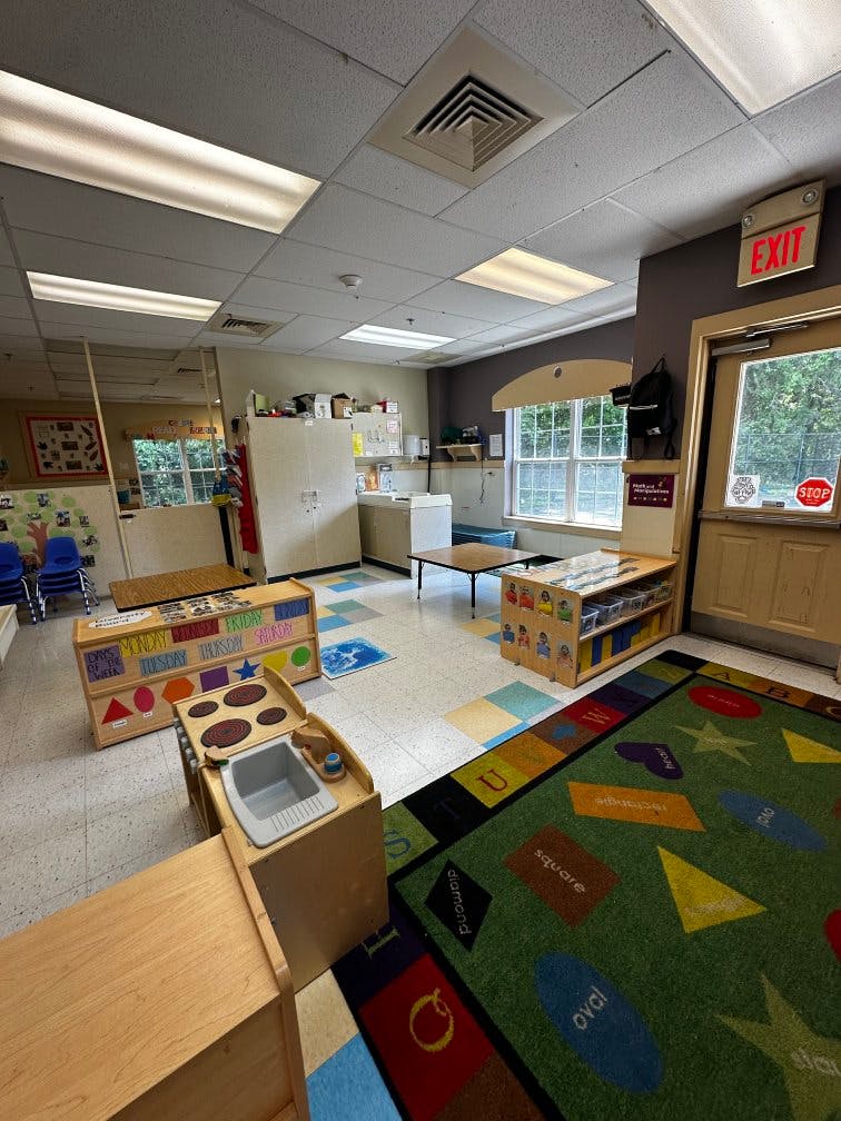 Classroom with toy kitchen, colorful rug with shapes, and an exit sign