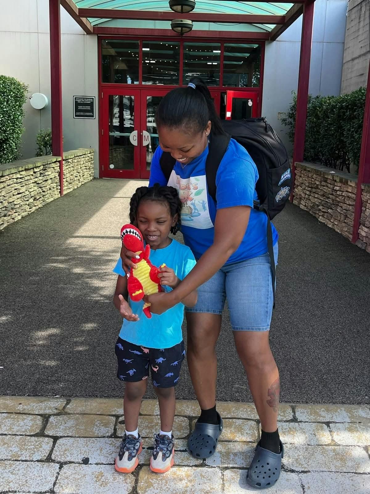 A person holding a toy dinosaur for a child outside a building
