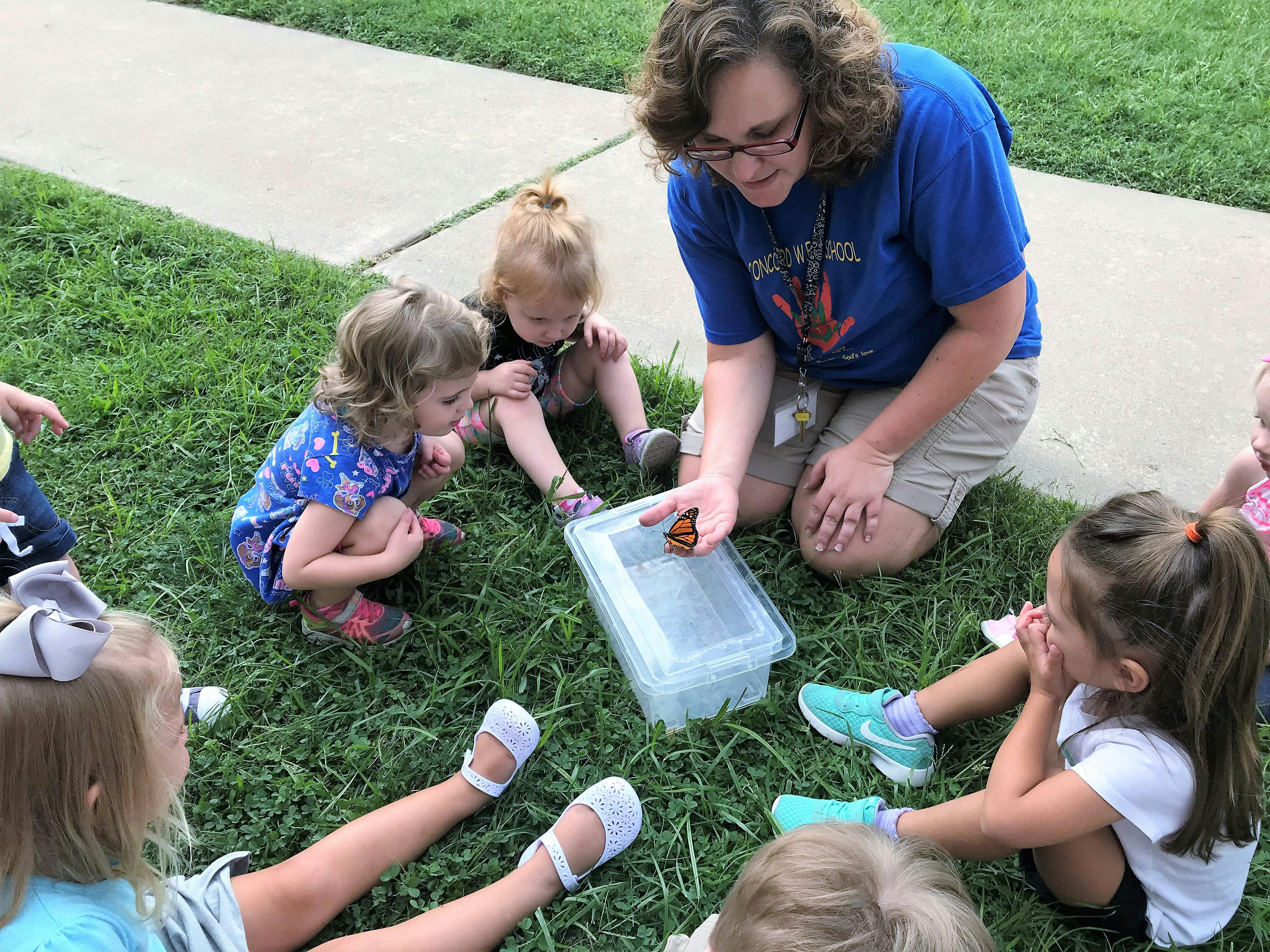 Adult and children on grass looking at an insect in a clear container