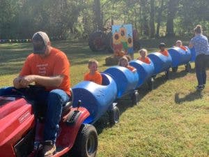 Person driving a tractor pulling children in blue barrel train cars