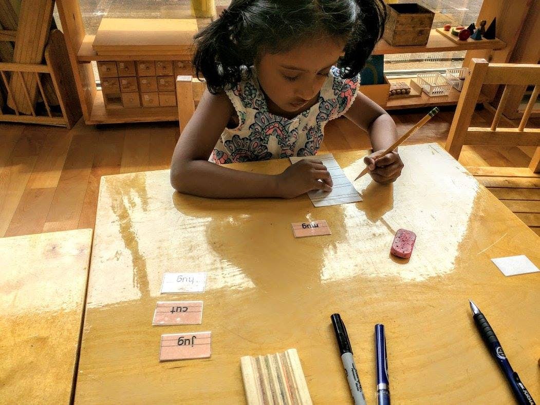 Child writing on paper at a table with a pencil