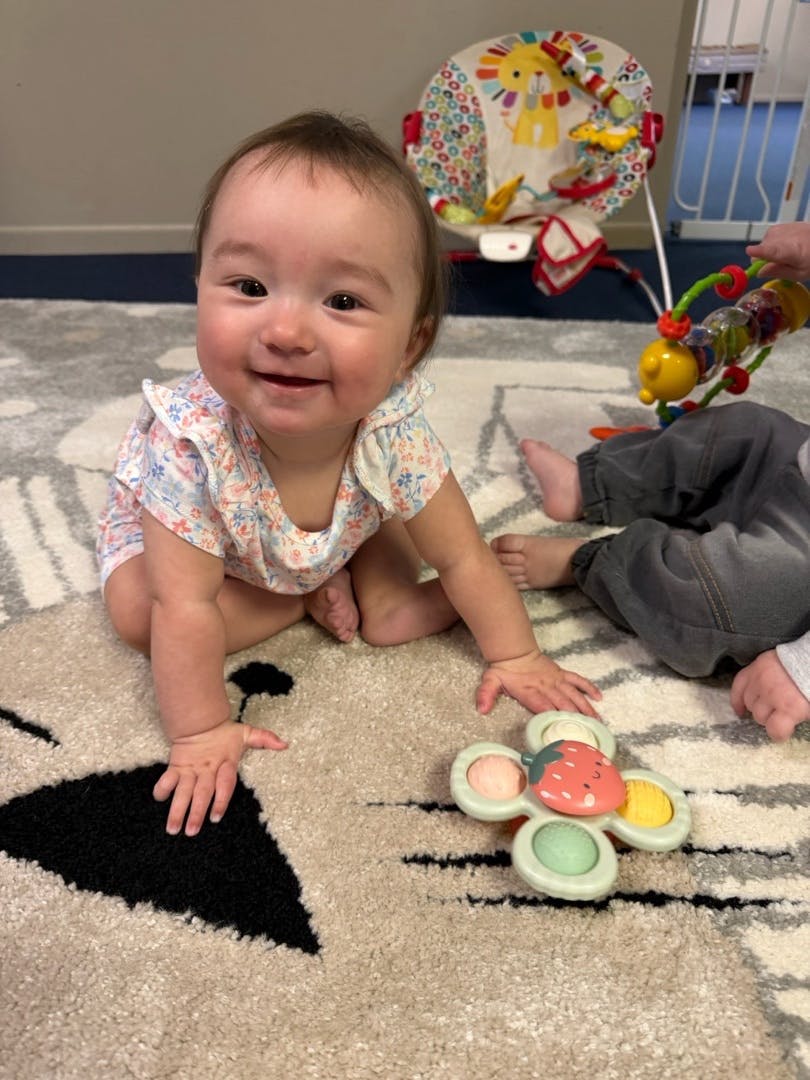 Smiling child sitting on a rug next to a strawberry toy