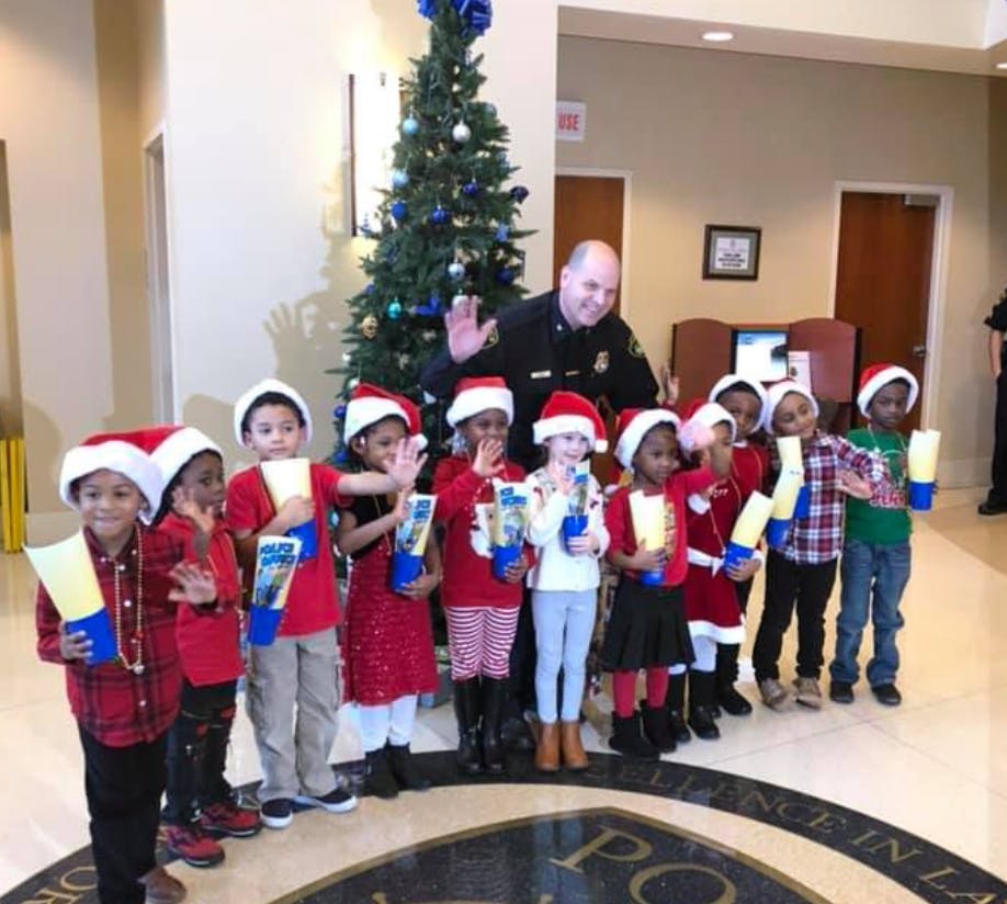 Adult and children in Santa hats holding gifts in front of a Christmas tree