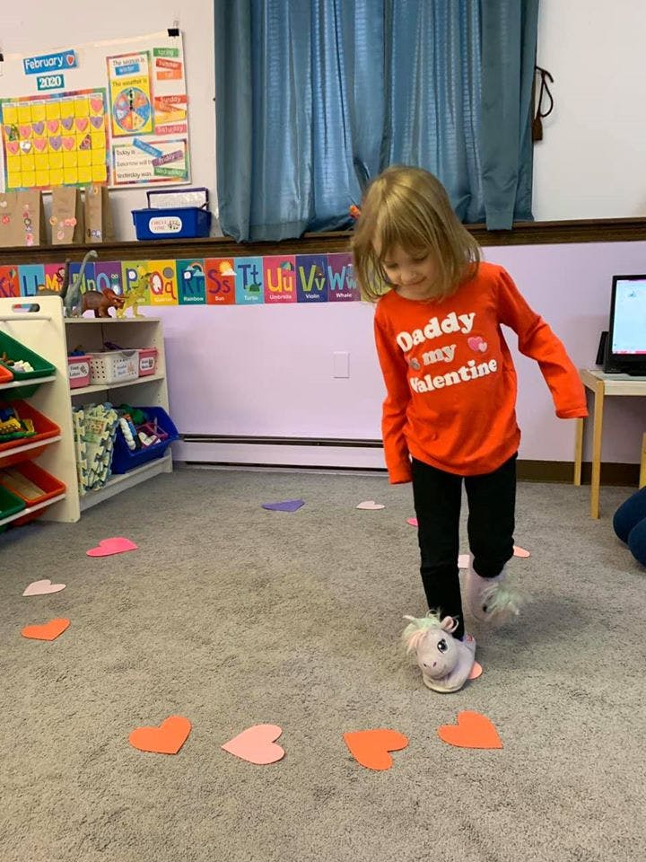 Child in orange shirt walking on heart cutouts on the floor
