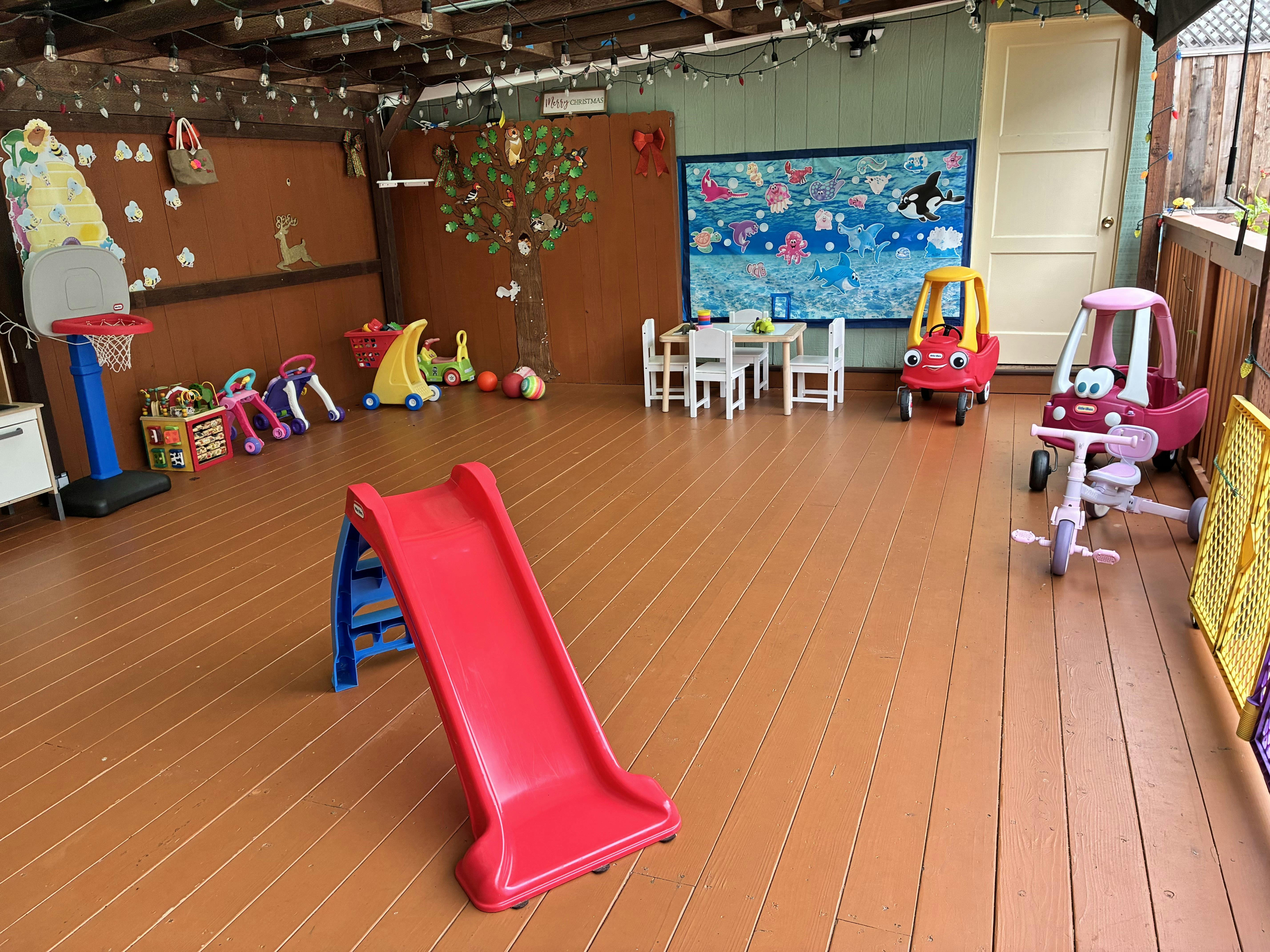 Children's play area on a wooden deck with a slide and various ride-on toys