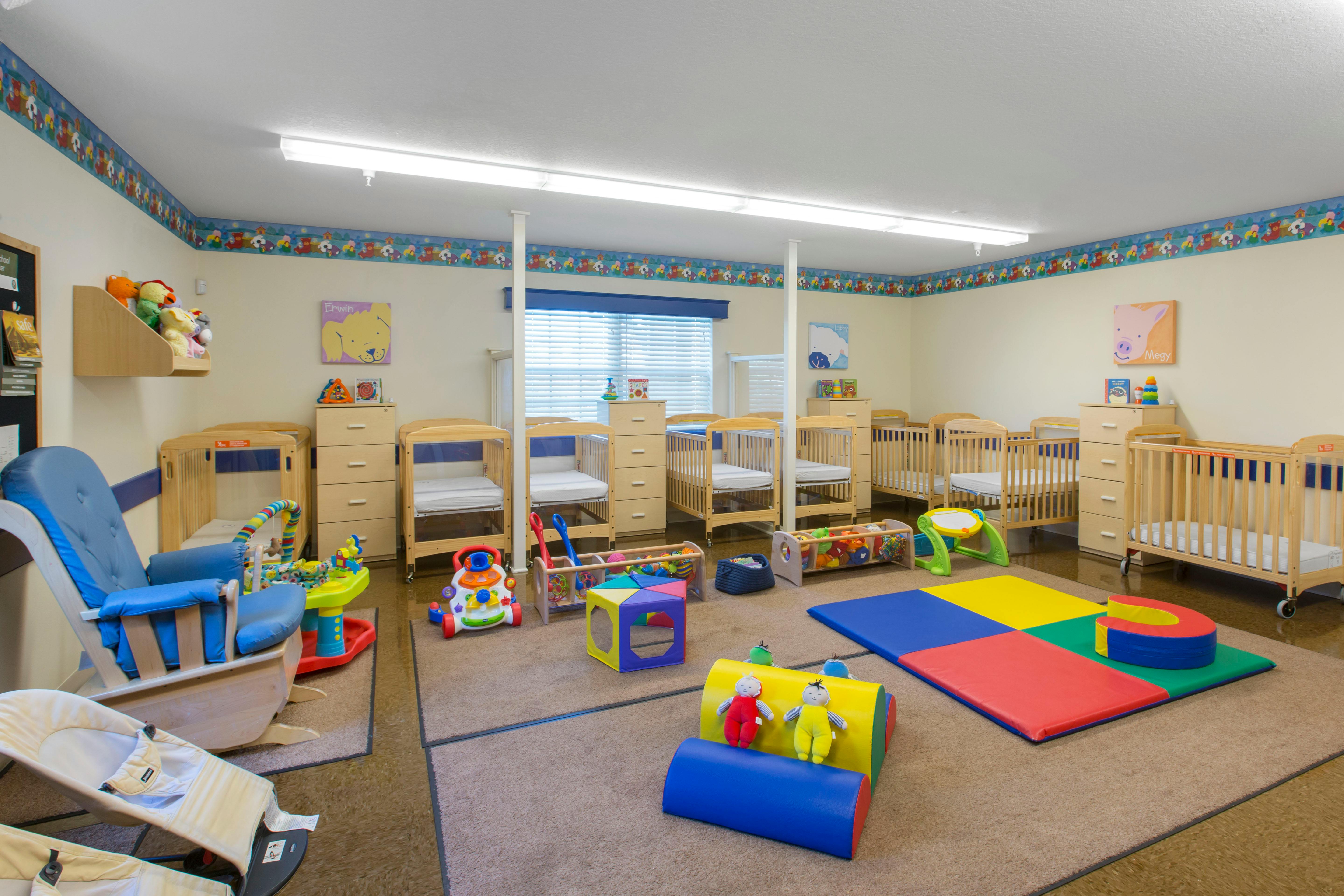 An empty nursery room with cribs, a rocking chair, and toys