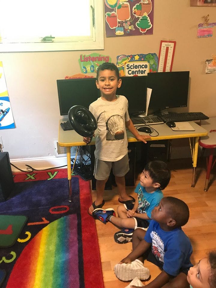 Child holding a black object while other children sit on the floor