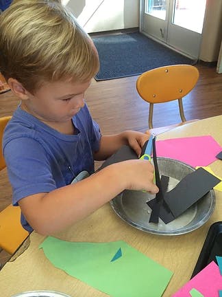 Child cutting black paper with scissors at a table