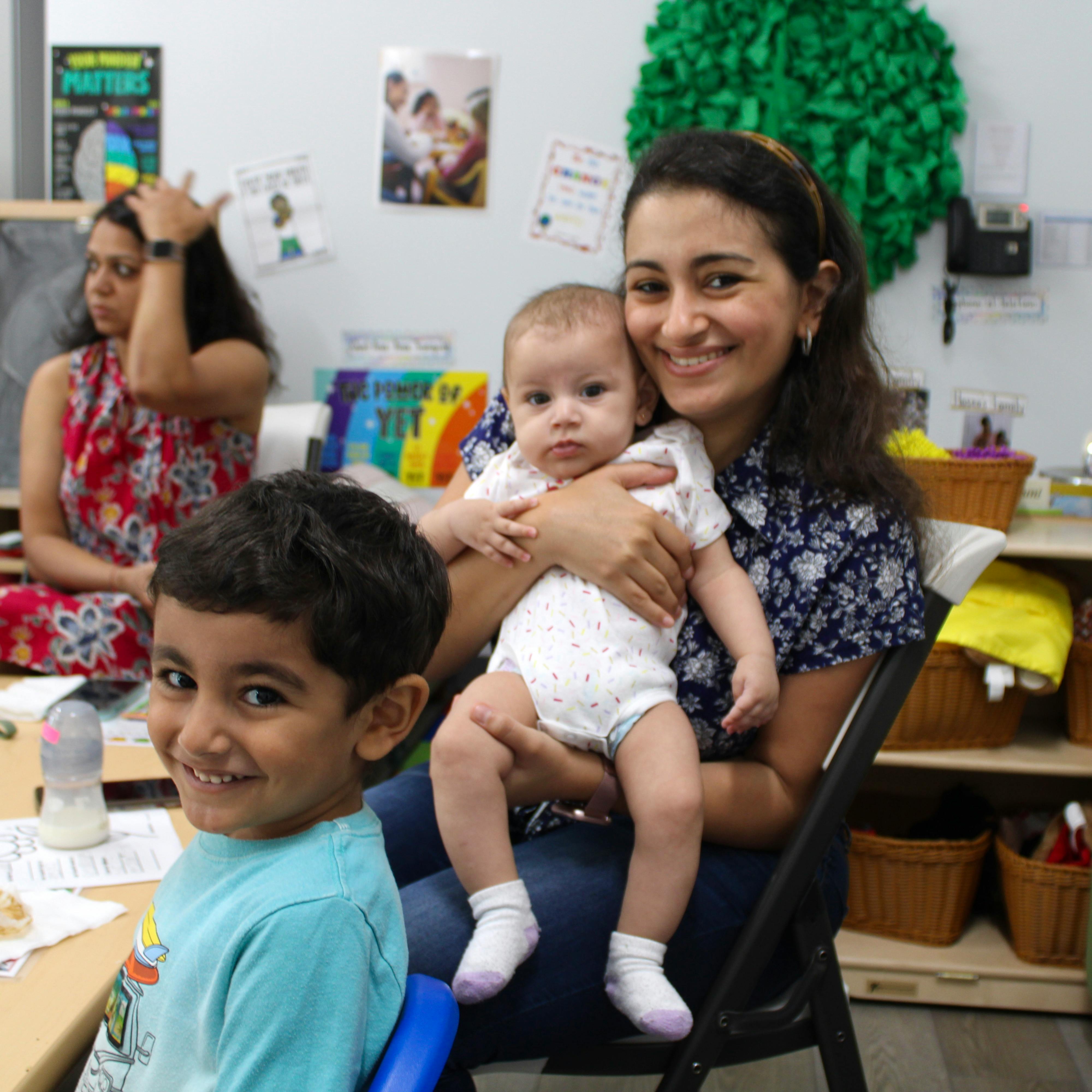 Person holding a baby, with a child smiling in the foreground