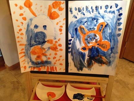 Two child paintings with blue and orange paint on an easel