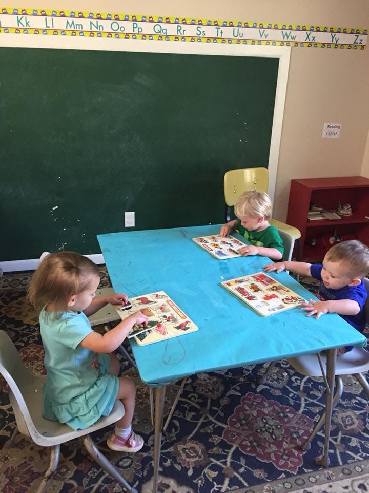 Three children playing with puzzles at a table in a classroom