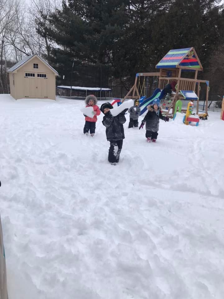 Children playing in snow with a play structure and shed in background