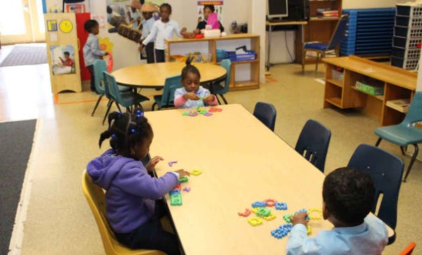 Children playing with colorful letters and shapes at tables in a classroom