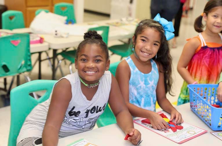 Two children smiling at a table, one playing with a puzzle