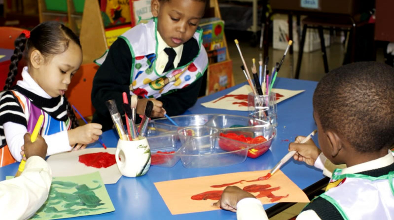 Three children painting at a table in a classroom