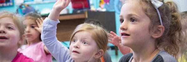 Children in a classroom, one child raising a hand
